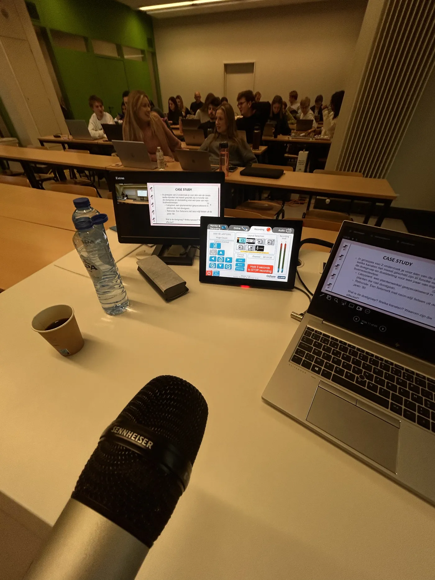 Zicht vanaf de docentenplek op een volle klas aan AP Hogeschool Antwerpen, met microfoon en laptop op de voorgrond
